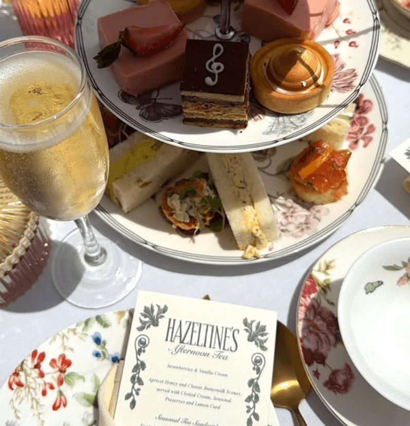 Elegant afternoon tea spread with tiered pastries, finger sandwiches, champagne, and floral patterned china.